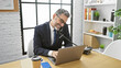© Krakenimages.com - Confident grey-haired hispanic man engaged in a business talk over the phone, working online in office