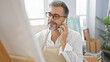 © Krakenimages.com - Handsome young hispanic artist with grey hair, engrossed in a vibrant phone conversation while confidently drawing at his bustling art studio.