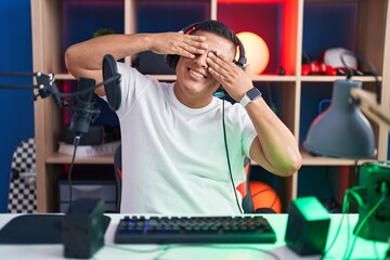 Canvas Print - Young hispanic man playing video games covering eyes with hands smiling cheerful and funny. blind concept.