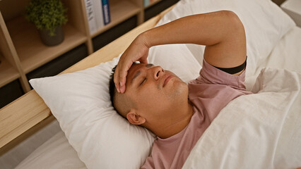 Canvas Print - Stressed young latin man lying in bed, worry seeping into his morning. bedroom indoors offering no relief from his headache, insomnia setting the room's tense backdrop.