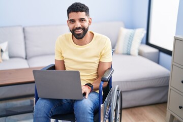 Canvas Print - Young arab man using laptop sitting on wheelchair at home