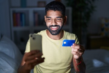 Wall Mural - Young arab man using laptop and credit card sitting on bed at bedroom