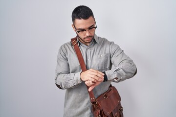 Wall Mural - Young hispanic man wearing suitcase checking the time on wrist watch, relaxed and confident