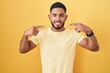 © Krakenimages.com - Young hispanic man standing over yellow background smiling cheerful showing and pointing with fingers teeth and mouth. dental health concept.