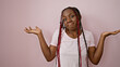 Clueless african american woman with braids, standing unsure over a pink isolated background, expressing doubt, confusion and indifference through her facial gestures