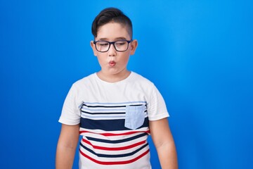 Sticker - Young hispanic kid standing over blue background making fish face with lips, crazy and comical gesture. funny expression.