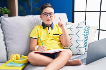 Wall Mural - Young hispanic kid doing homework sitting on the sofa pointing finger up with successful idea. exited and happy. number one.