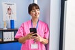 Young beautiful hispanic woman physiotherapist smiling confident using smartphone at rehab clinic