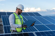 © Alan - professional engineer using a laptop in front of a solar panel power station, handsome male technician electrician looking at the screen holding a computer