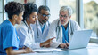© MP Studio - Focused group of medical professionals, including three doctors and nurses, gathered around a laptop, discussing or reviewing something of importance.