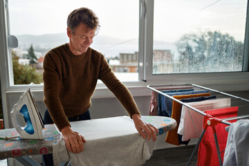 Wall Mural - Mature man ironing clothes at home. The concept of maintaining cleanliness and taking care of health.