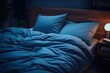  a bed with a blue comforter and pillows in a room with a lamp on the side of the bed.