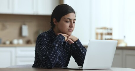 Canvas Print - Thoughtful positive young Indian freelancer woman using laptop at kitchen table, working at home workplace, thinking on Internet project at computer, typing, making decision, looking at display