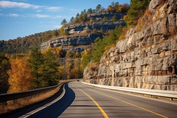 Wall Mural -  a car driving down a road in front of a mountain side with fall colored trees on the side of the road.