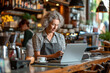 Middle aged woman small business owner working with laptop computer behind the counter bar in a cafe making order