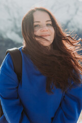 beautiful overweight brunette woman in a blue hoodie against the background of mountains in winter