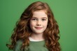 Portrait of a cute little girl with long red curly hair on a green background