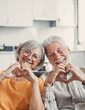 © Daniel - Close up portrait happy sincere middle aged elderly retired family couple making heart gesture with fingers, showing love or demonstrating sincere feelings together indoors, looking at camera..
