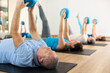 Willing aged man engaging in pilates training with ball in gym room during workout session. Persons practicing pilates in fitness studio