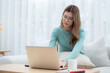 © N_studio - Young asian woman wearing glasses sitting sofa working on laptop computer in living room at home, woman work from home with telework, freelance working at workspace, business and digital life.