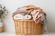 A wicker laundry basket filled with folded warm blankets in neutral tones on a light background, suggesting home comfort.