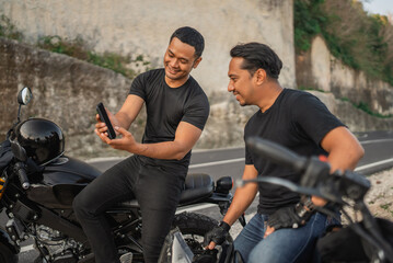 Canvas Print - asian rider watching handphone together while sitting on motorcycle outdoors