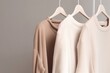 Neutral-toned clothes on hangers against a gray background, minimalist fashion concept.