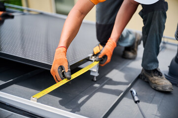 Wall Mural - Worker building solar panel system on rooftop of house for generating electricity through photovoltaic effect. Close up man using ruler to measure mounting equipment for precise installation.