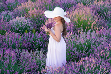 glad girl in white dress walking through lavender flowers. lovely girl posing in lavender flowers. beautiful girl in lavender field surrounded by flowers. teenage girl at lavender flowers in garden