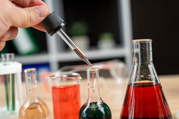 close up hand with pipette dripping liquid to test tube in laboratory