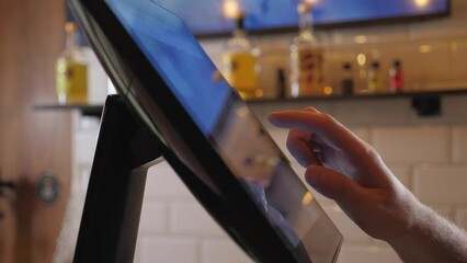 Close-up of the waiter's or bartender's hands on the touch screen in the cafe, he takes the customer's order. The bartender swipes his finger across the touch screen while making out an invoice.