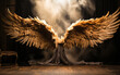 Imposing bronze angel wings open wide in a dramatic display, set against a moody theatrical backdrop with a mystical foggy glow