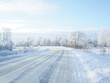 © Nekrasov - A country road leading among frozen trees on a sunny winter day. Frost-covered frozen trees on the edge of a winter snow-covered country road.