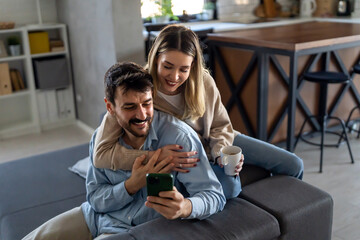 Wall Mural - Smiling couple embracing while looking at smartphone. People sharing social media on smart phone.