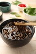 Eating delicious buckwheat noodle (soba) soup with chopsticks at white wooden table, closeup