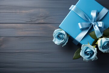  a blue gift box with a blue ribbon and two white roses on a gray wooden background with a blue bow.