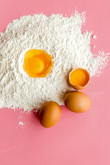 Baking background with eggs and flour on pink table. Top view.