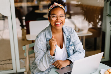 Happy young woman working in a cozy cafe with laptop