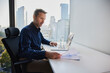 © Westend61 - Mature businessman examining documents and sitting with laptop at desk