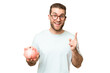 © luismolinero - Young man holding a piggybank over isolated chroma key background pointing up a great idea