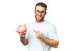 © luismolinero - Young man holding a piggybank over isolated chroma key background and pointing it