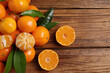 Fresh tangerines with green leaves on wooden table, top view. Space for text