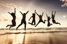 Group Of Silhouettes Of Happy Young Friends Are Having Fun And Jumps Together At Sunset Sea Beach