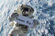 © Keitma - Dream big concept image with an astronaut in space holding a board sign with written words Dream Big