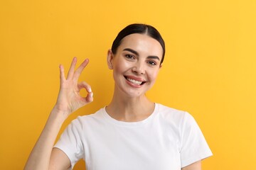 Wall Mural - Beautiful woman with clean teeth smiling and showing OK gesture on yellow background