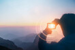 Silhouette of a person capturing sunlight in their hand during a beautiful mountain sunrise, creating a magical effect..