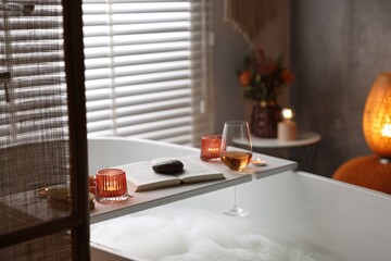 Wall Mural - White wooden tray with glass of rose wine, book and burning candles on bathtub in bathroom