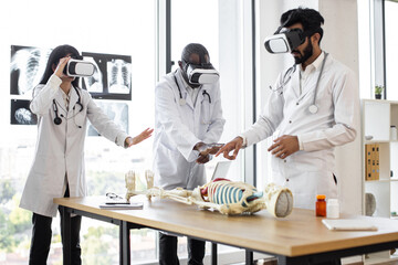 Young multiethnic doctors, bioengeneers, scientists with virtual reality equipment vr goggles in the laboratory working with human skeleton anatomy.