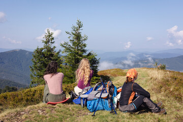 Wall Mural - a group of girls tourists are sitting on a pass in the mountains against the backdrop of a beautiful