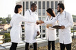 © sofiko14 - Group of diverse doctors in white medical coats meeting during break outdoors on rooftop terrace hospital , greeting each other by shaking hands.